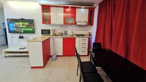 A compact kitchen with red and white cabinets, a microwave, a sink, and a stove. There is a TV mounted on the wall displaying a show. - 5 minutes walk from sea family apartment (Batumi)