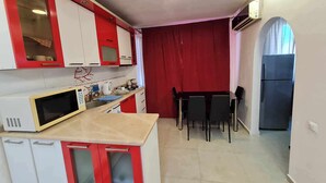 A compact kitchen with red and white cabinets, a microwave, a sink, and a dining area with a table and chairs. - 5 minutes walk from sea family apartment (Batumi)
