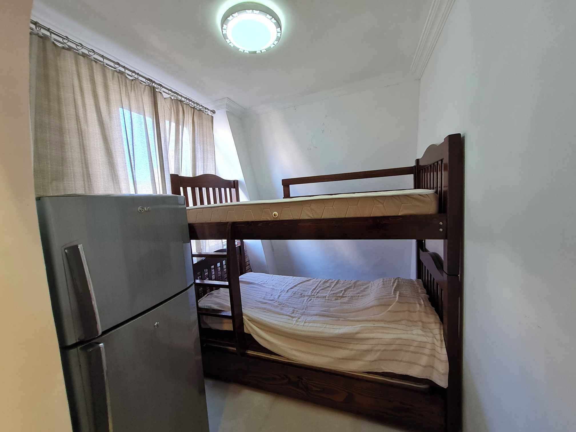 A small room with a bunk bed, a refrigerator, and a window with curtains.