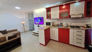 A compact kitchen with red and white cabinets, a microwave, stove, and a TV mounted on the wall. - 5 minutes walk from sea family apartment (Batumi)