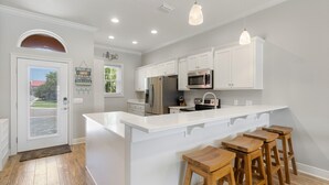 A modern kitchen with white cabinetry, stainless steel appliances, and a central island with bar stools. - Coastal Living Perfected: Banana Bay's Intracoastal Retreat with Sandy Shores (Pensacola)