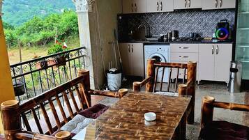 Un espace repas avec une table et des chaises, une cuisine équipée de placards et d’appareils électroménagers, et une vue sur la verdure à travers une arche.