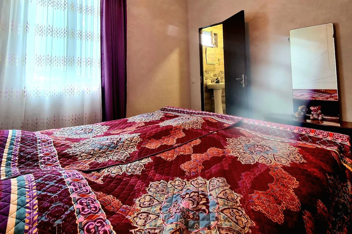 Un dormitorio con una cama grande, una lámpara colgante, una ventana con cortinas y un espejo en la pared.
