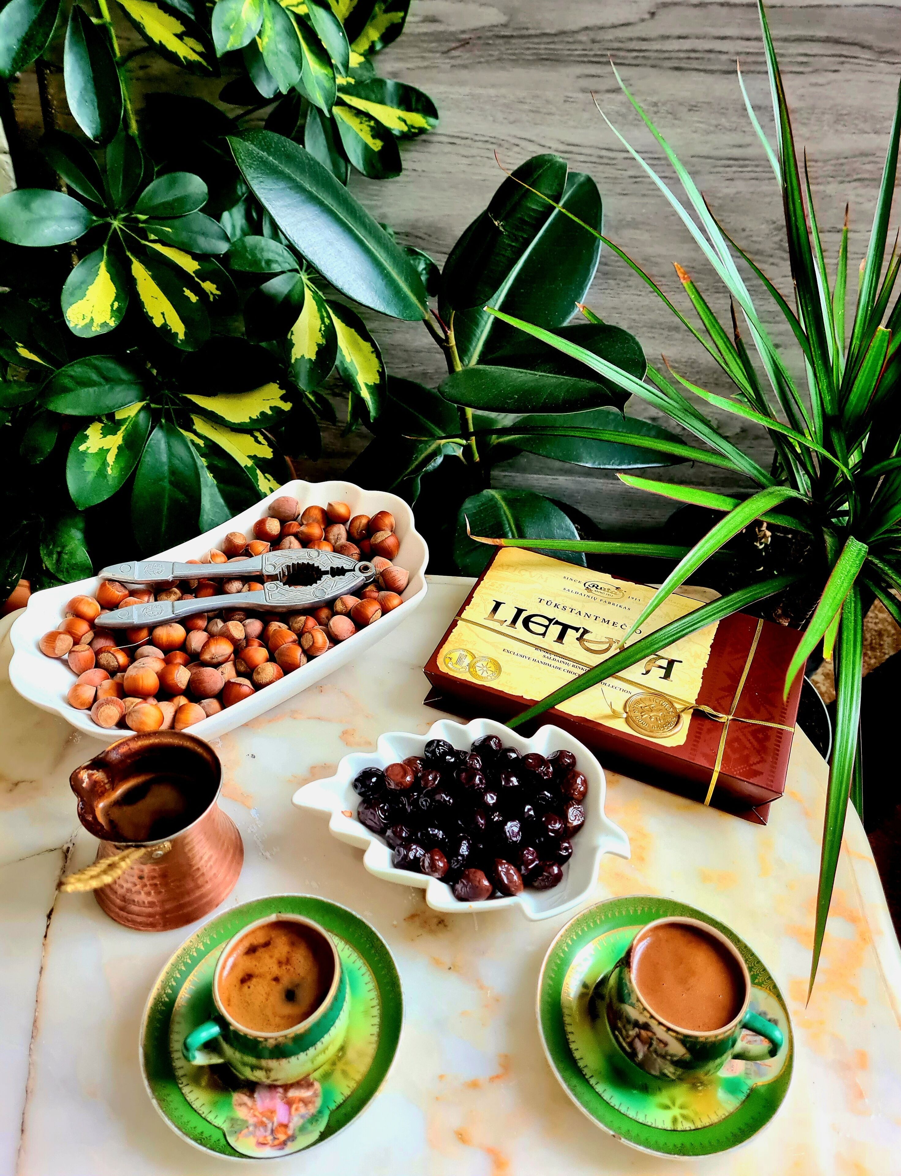 Una mesa con avellanas, una caja de bombones, un bol de cerezas y dos tazas de café.