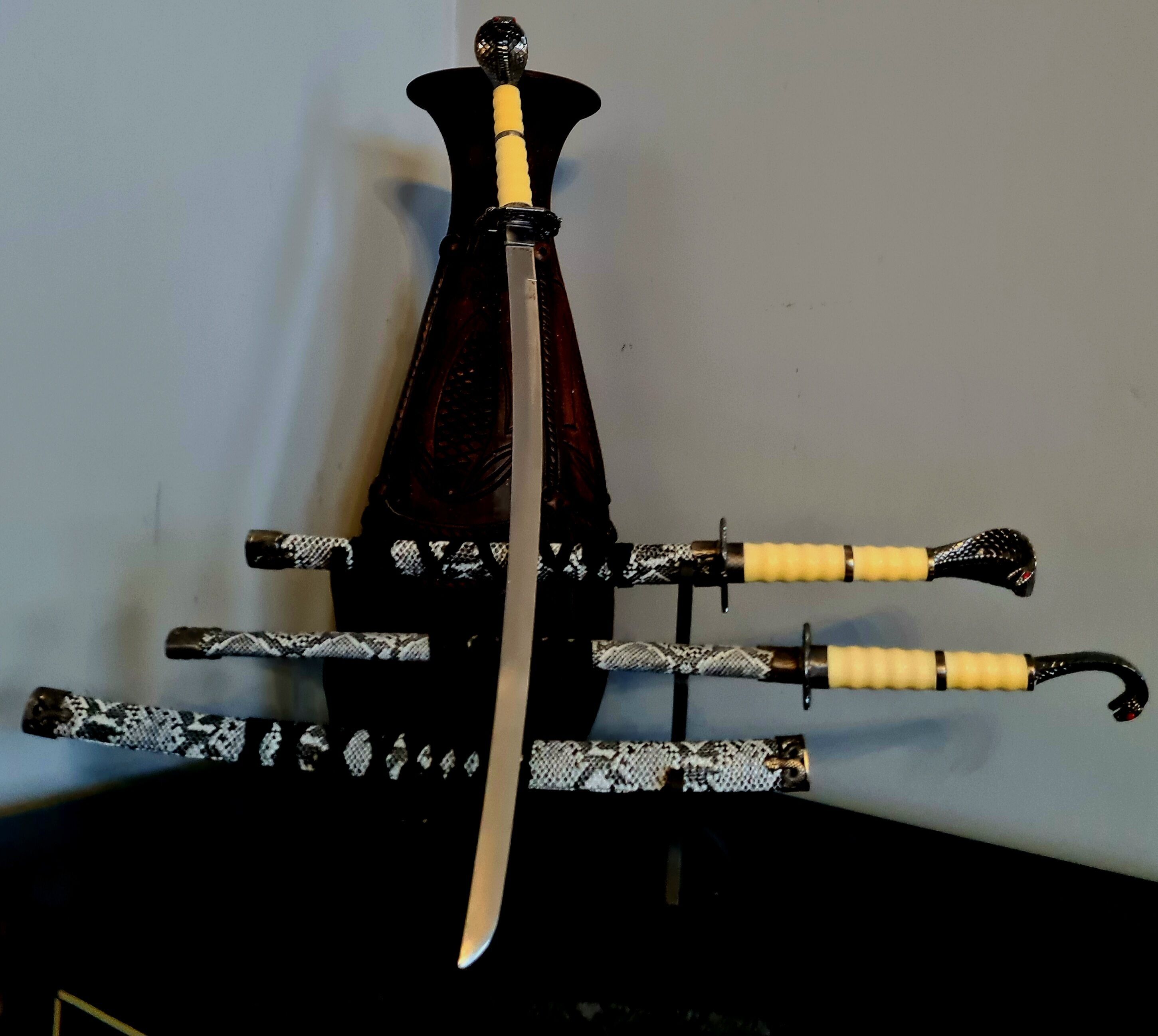Una espada con empuñadura de asta y blanco, un agarre amarillo y un pomo negro, montada sobre un soporte con base de patrón blanco y negro.