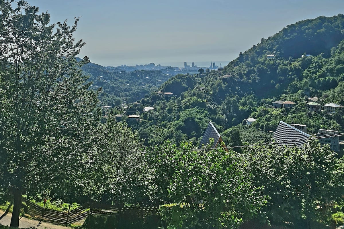 Un paisaje verde y exuberante con vistas a una ciudad a lo lejos, un camino y un edificio de techo inclinado.