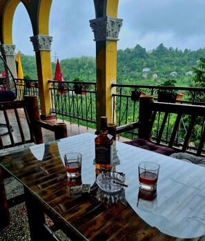 A table with a bottle of Jack Daniel's whiskey, two glasses, and an ashtray. The table is set outdoors with a view of a lush green landscape. - Old House korolistavi (Khelvachauri)