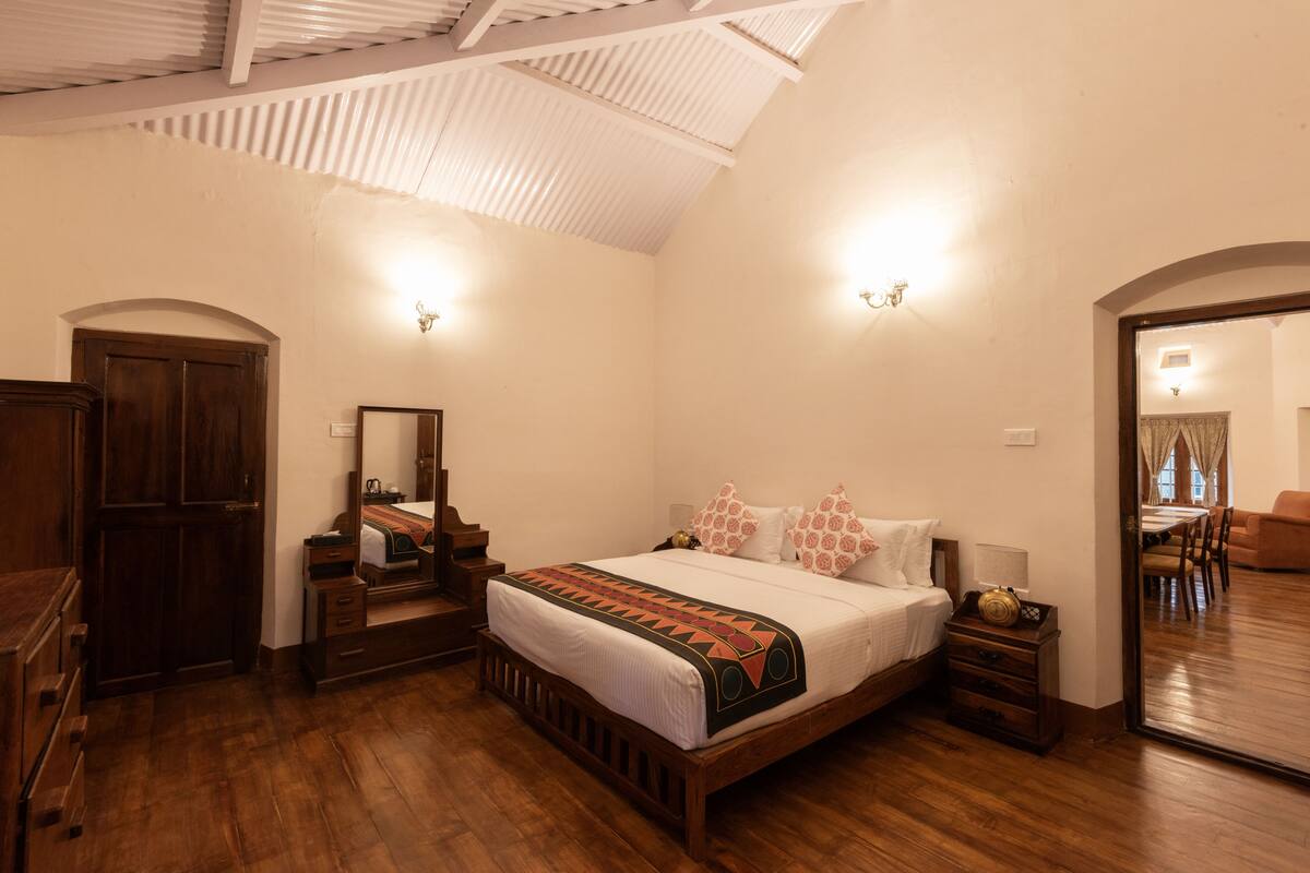 A bedroom with a wooden bed, a dresser, a mirror, and a door leading to another room.