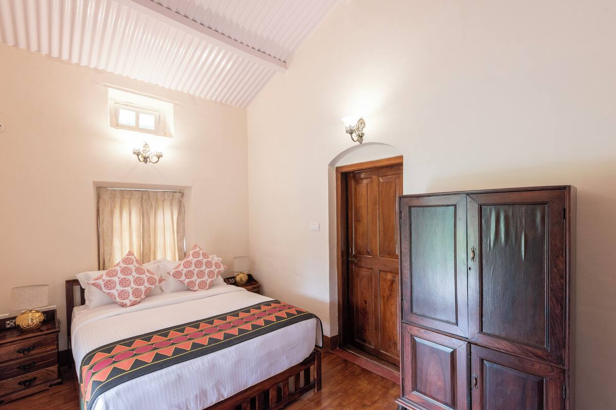 A bedroom with a bed, wooden wardrobe, and a window with curtains.