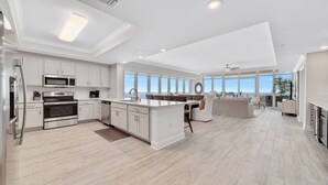 Une cuisine spacieuse avec des meubles blancs, un îlot central et une vue sur l’extérieur.