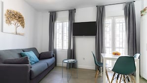 Una sala de estar moderna con un sofá gris, una mesita redonda y un comedor con una mesa blanca y sillas verdes.