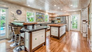 A spacious kitchen with wooden cabinets, a central island, and bar stools. - AMBER COTTAGE ~ Renovated 3 Bedroom, 3.5 Bathroom Home w/ Pool! (Key West)