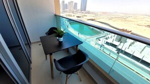 A balcony with a glass railing, a small table with a potted plant, and a black chair. - Pristine Studio with Canal View - 703 (Abu Dhabi)