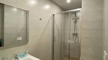 Un baño moderno con ducha de vidrio, un lavamanos con espejo y un inodoro.