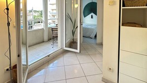 Una habitación con puerta corrediza de vidrio que da a un balcón, una cama con un ventilador verde y un estante blanco con cestas.