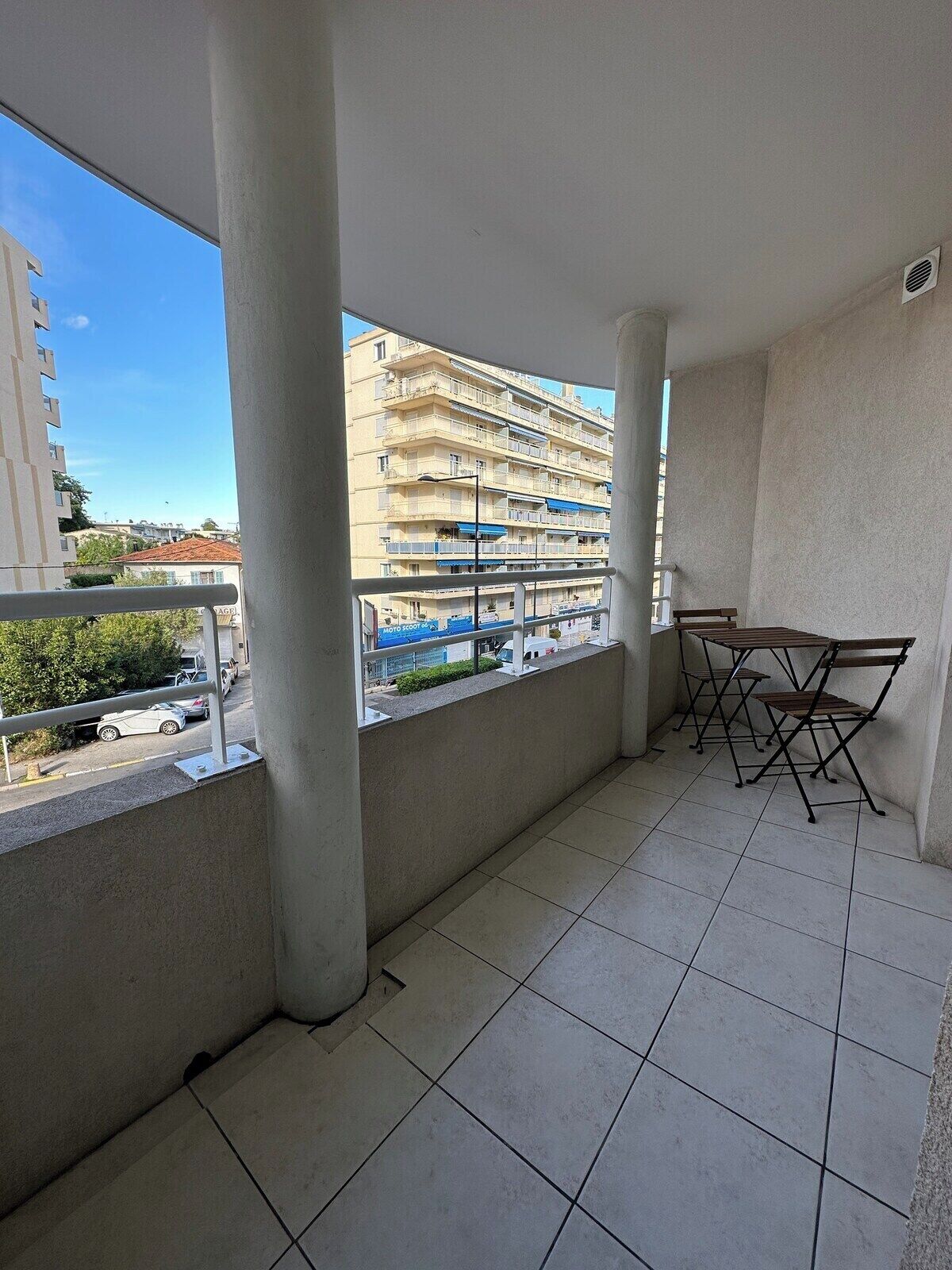 Un balcon avec un sol carrelé, une table avec des chaises et une vue sur un immeuble à plusieurs étages.