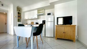 Una cocina moderna con armarios blancos, un microondas integrado, un refrigerador y un mueble de madera con un televisor.