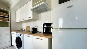 Una cocina moderna con armarios blancos, lavadora integrada, cafetera y refrigerador.