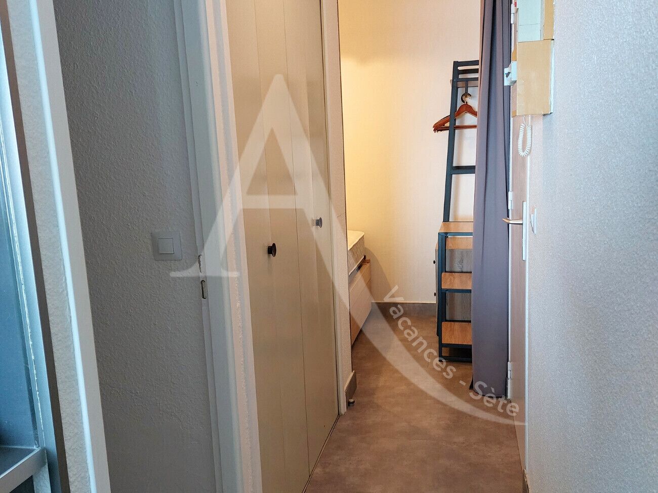 Un pasillo estrecho con una puerta a la izquierda, una escalera de madera apoyada contra la pared a la derecha y un pequeño estante con un teléfono.