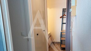 En smal hall med en dörr på vänster sida, en trästege som står lutad mot en vägg på höger sida och en liten hylla med en telefon.