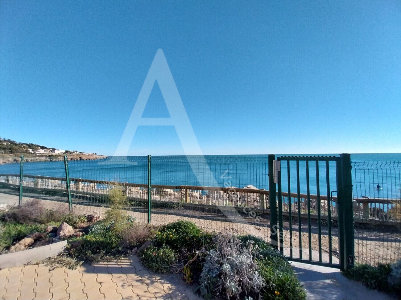 Ein Küstenweg mit einem Metallzaun, der zu einem Strand mit freiem Blick auf das Meer führt.