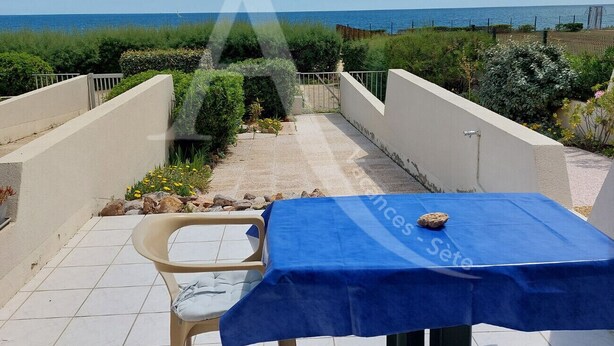 Um terraço com mesa coberta por um tecido azul, uma cadeira e vista para o mar.