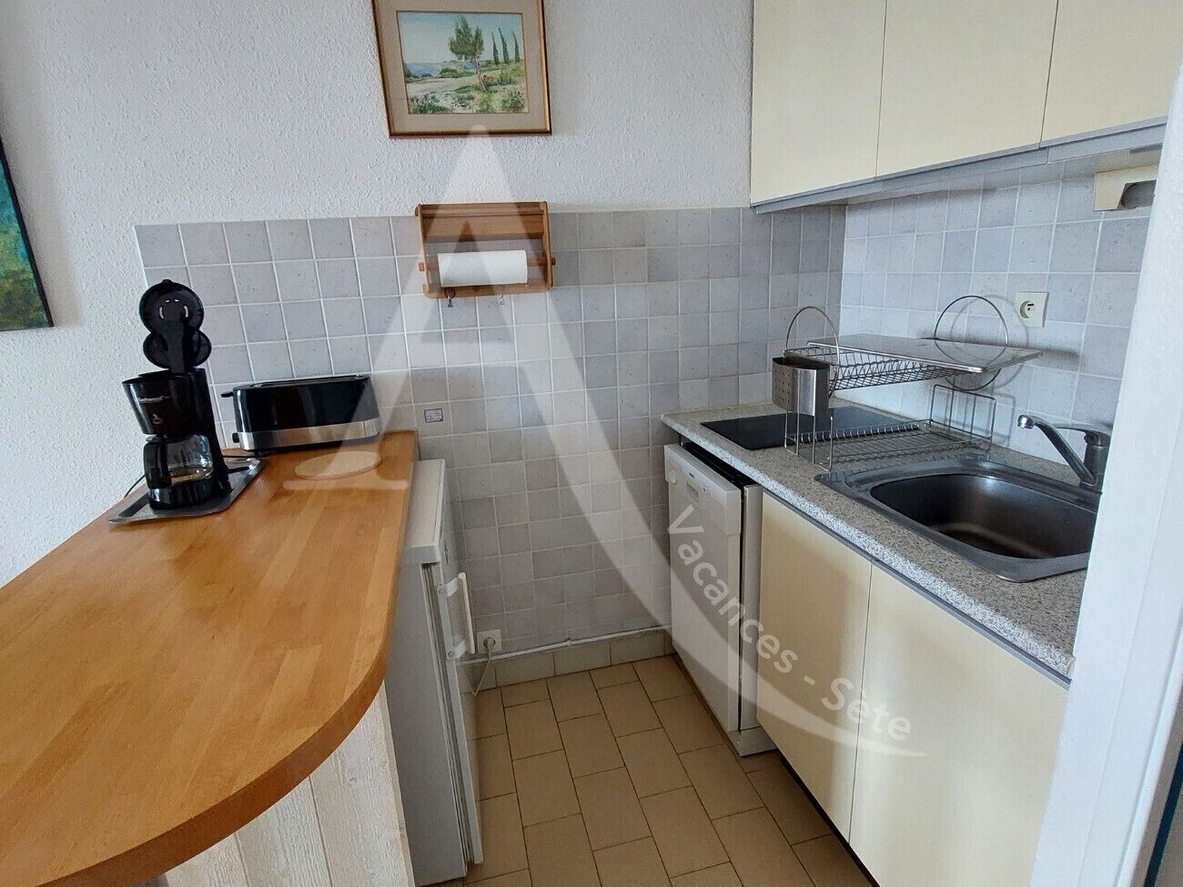 A compact kitchen with a wooden countertop, a coffee maker, a dishwasher, and a sink.