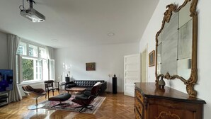 A spacious living room with a wooden parquet floor, a black leather sofa, a coffee table, and a large ornate mirror on the wall. - Zagreb Center 2BR + 2.5BA - 104m² Loft by Cathedral (Zagreb)