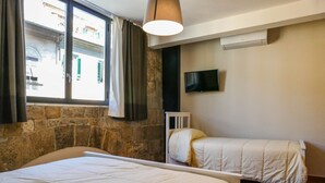 A bedroom with two beds, a window with curtains, a TV on the wall, and an air conditioning unit. - Gialel Pisa Guest House (Pisa)
