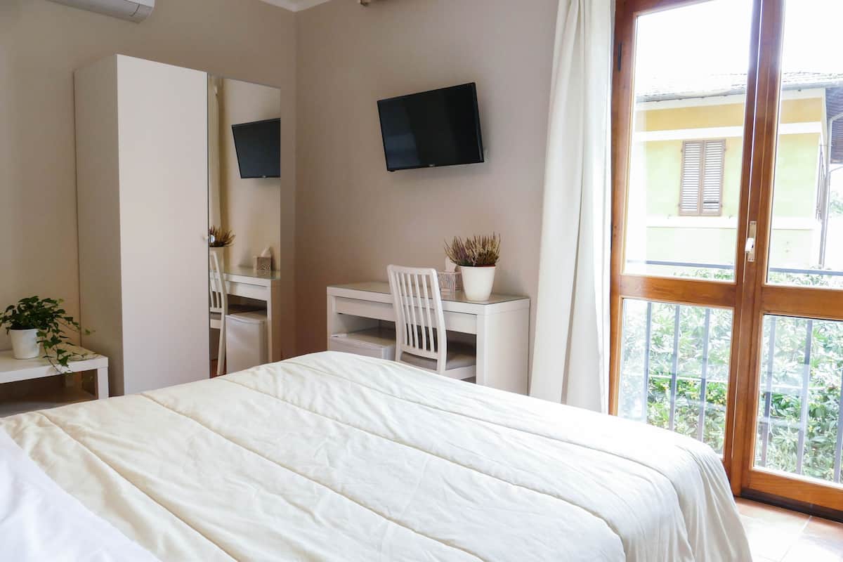 A bedroom with a bed, a desk, a chair, a TV, and a balcony with a view.