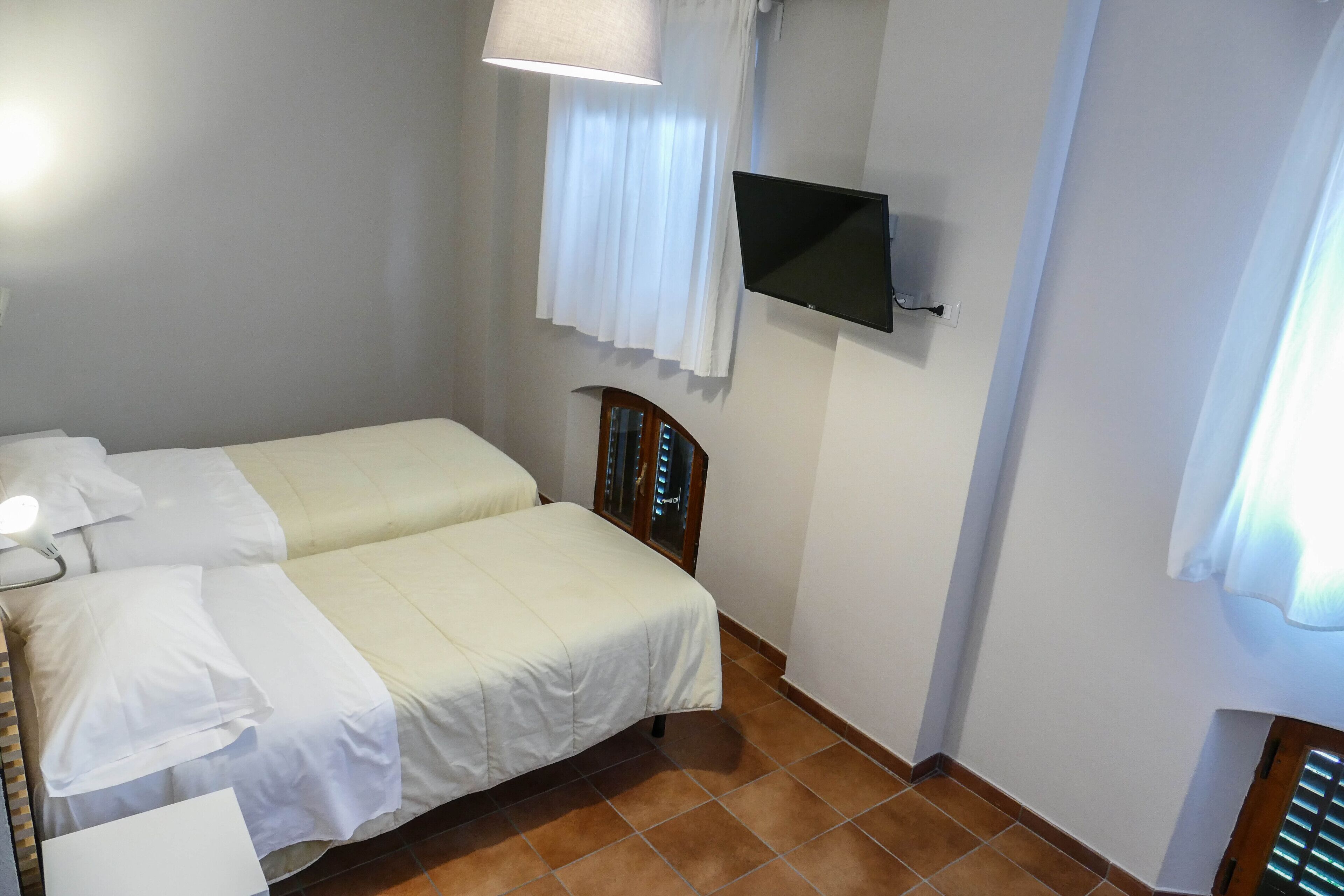 Un dormitorio con dos camas, un televisor montado en la pared y un ventanal con cortinas.