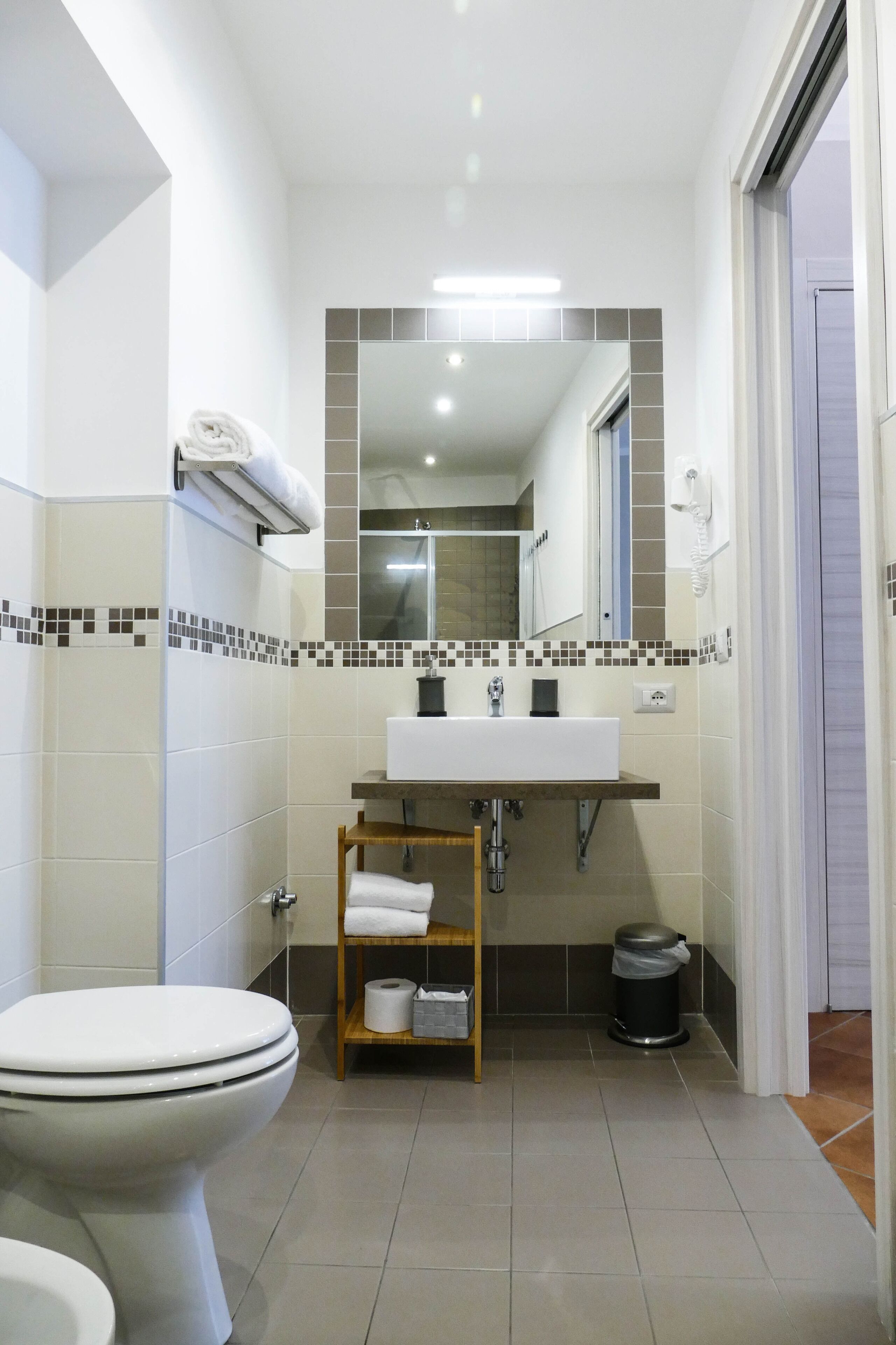 Un baño con inodoro, lavamanos, espejo y paredes revestidas con azulejos.