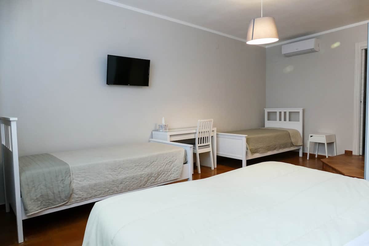 A bedroom with two single beds, a desk, a chair, a TV, and an air conditioning unit.