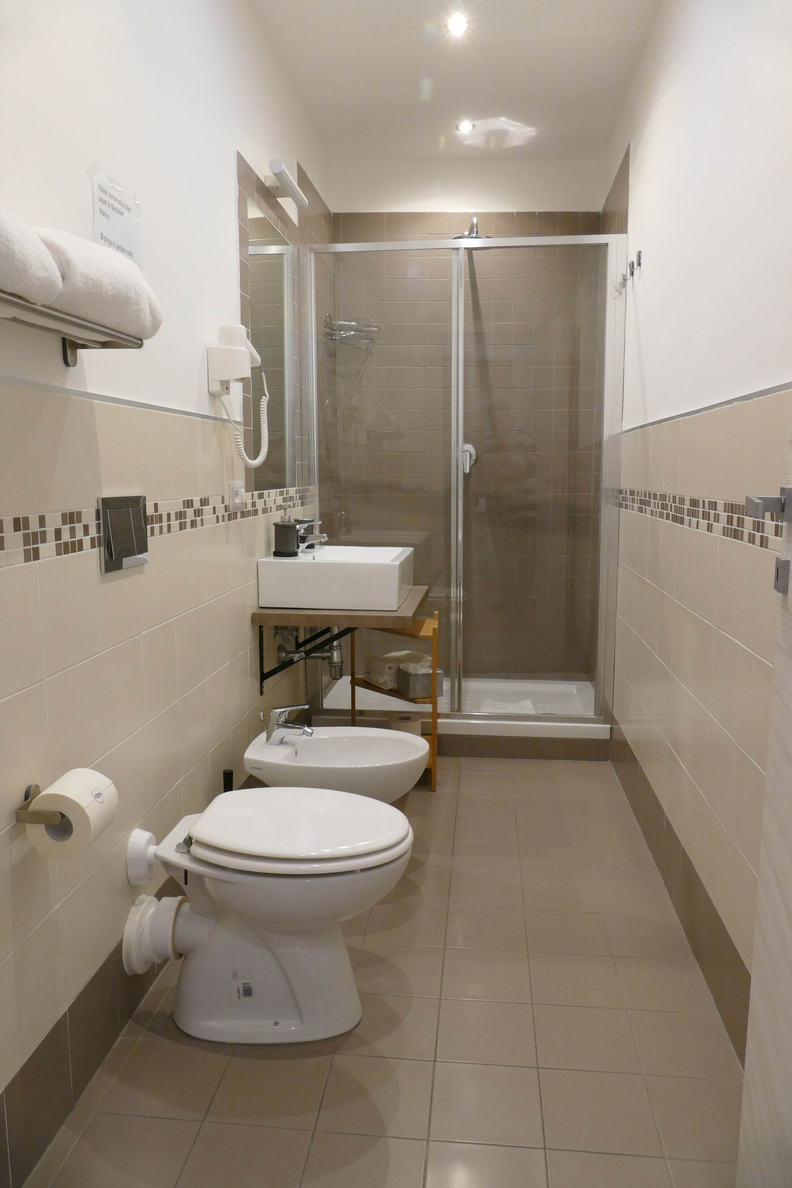A modern bathroom with a toilet, bidet, sink, and glass-enclosed shower.