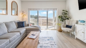 Un salon moderne avec un canapé, une table basse et une vue sur un balcon extérieur, accessible par une grande porte-fenêtre coulissante.