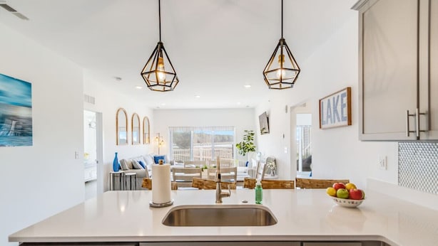 Une cuisine moderne dotée d’un îlot central, d’appareils électroménagers en acier inoxydable et de luminaires suspendus.