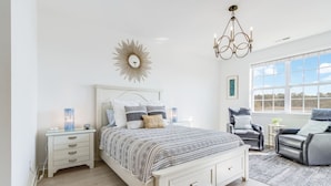 Une chambre à coucher avec un grand lit, des tables de chevet, un lustre et une vue sur l’extérieur grâce à de grandes fenêtres.