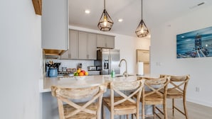 Une cuisine moderne avec des chaises en bois, un coin café et un tableau représentant un phare.