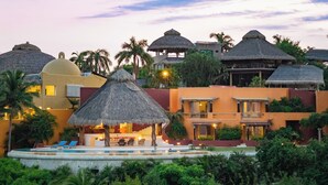 Un resort con varias construcciones de techo de paja, una piscina y abundante vegetación.
