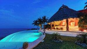 Un resort con piscina, edificio de techo de paja y palmeras.