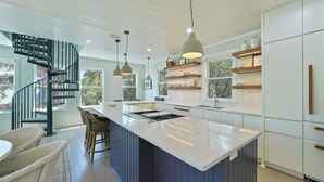 Uma cozinha moderna com ilha central, iluminação pendente e escada em espiral.