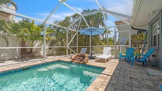 A pool with clear water, surrounded by a covered patio with chairs and a table. - Beached Inn 3 Bedroom Home by RedAwning (Holmes Beach)
