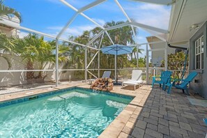 Une piscine à l’eau claire, entourée d’une terrasse couverte avec des chaises et une table.