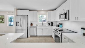 A modern kitchen with white cabinetry, stainless steel appliances, and a central island. - Beached Inn 3 Bedroom Home by RedAwning (Holmes Beach)