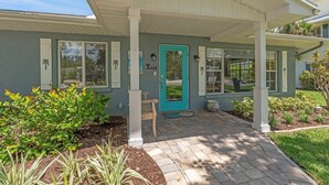 A house with a covered porch, a teal door, and a number 218 on the wall. - Beached Inn 3 Bedroom Home by RedAwning (Holmes Beach)