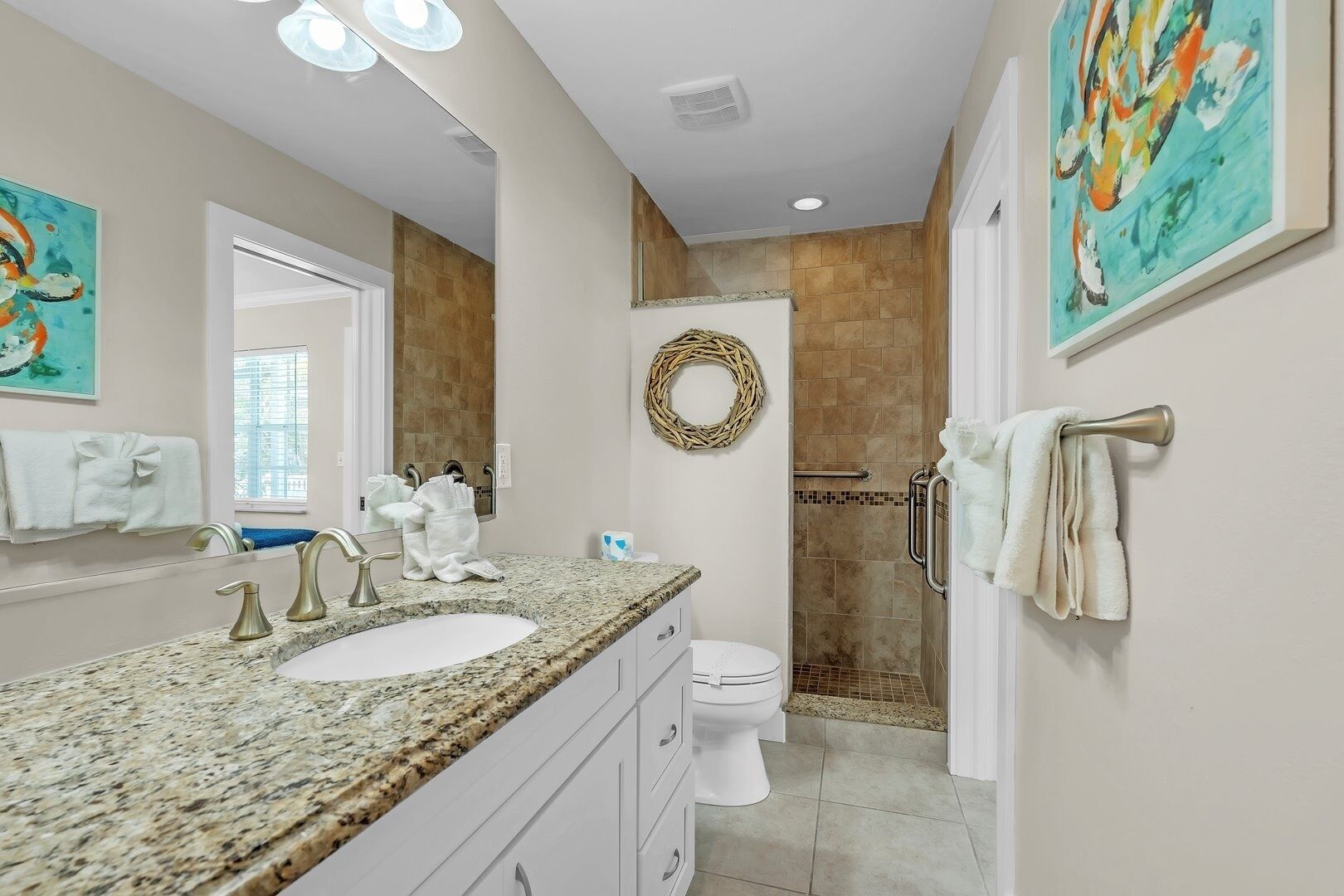A bathroom with a granite countertop, two sinks, a toilet, and a shower area.