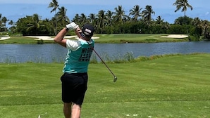 A golfer on a golf course with a water body and palm trees in the background.