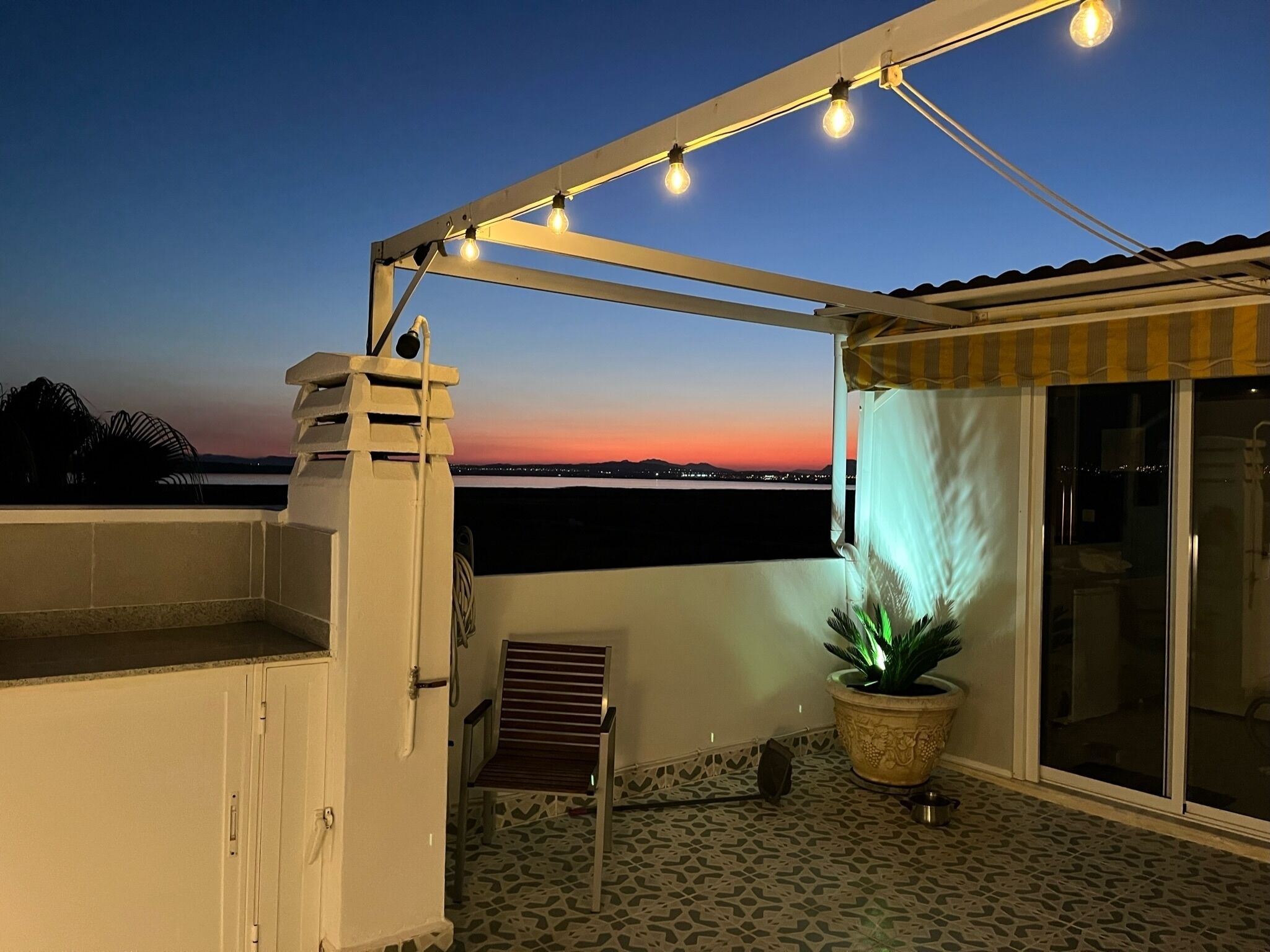 Een balkon met uitzicht op de zonsondergang, een bloempot en een stoel.