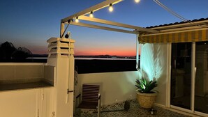 A balcony with a view of the sunset, a potted plant, and a chair.