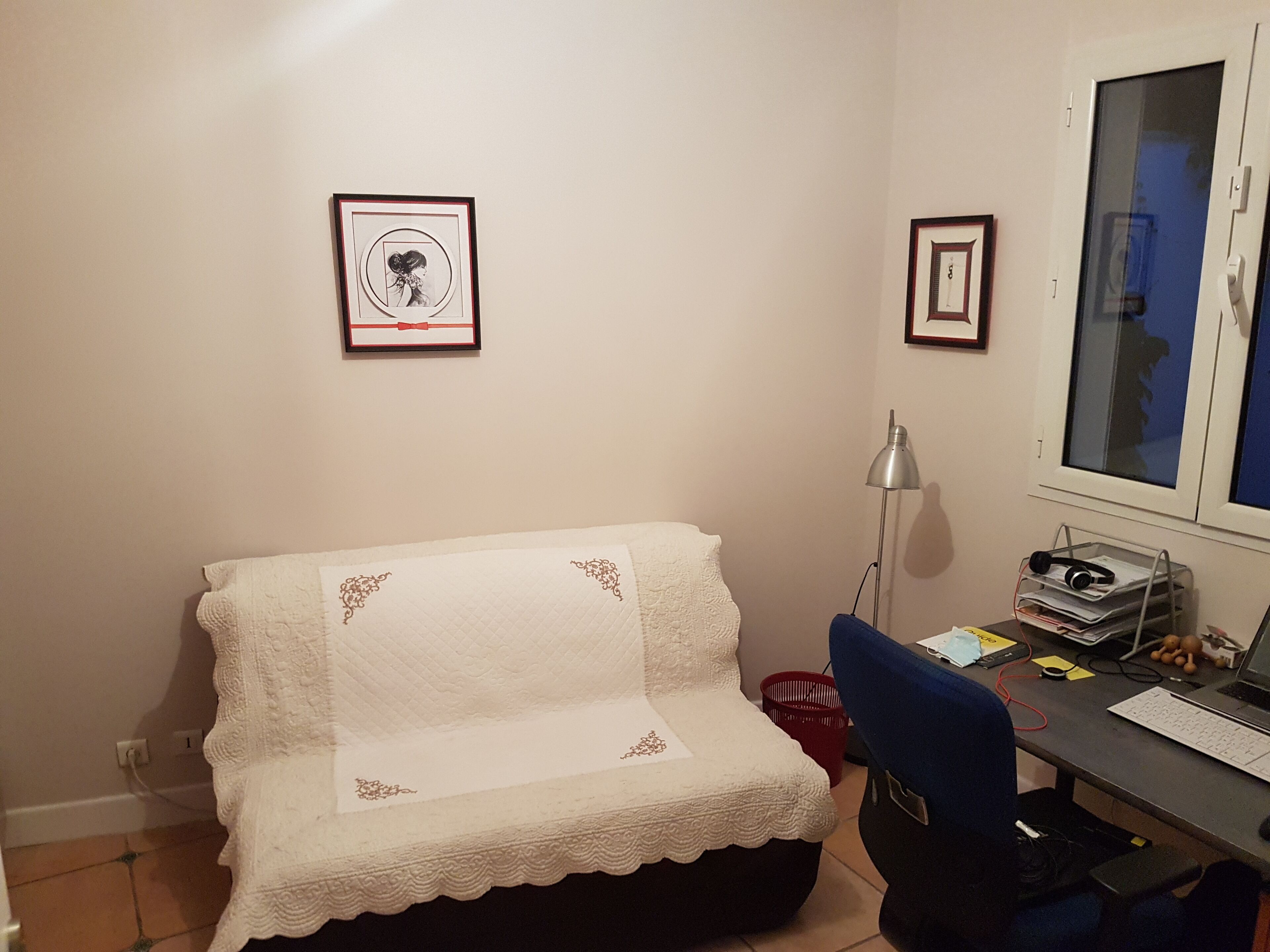 Ein kleiner, gemütlicher Raum mit einem Bett, einem Schreibtisch und einem Computer. An den Wänden hängen Bilderrahmen, es gibt eine Lampe und ein Fenster mit Blick.